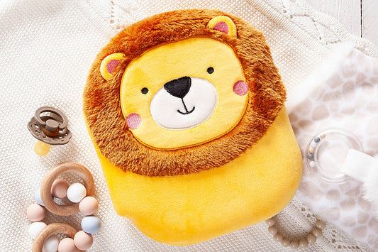 The Squish and Snugg Lion Book by BroadStreet Publishing Group, LLC, featuring a friendly lion with a plush, soft face, rests on a white knit blanket beside a pacifier, wooden teething rings with beads, and a patterned cloth.