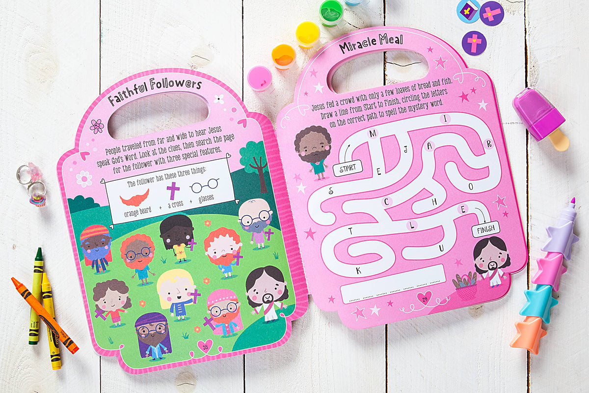 Two colorful My Pretty Pink Bible Activity Book activity sheets from BroadStreet Publishing Group, LLC, featuring cartoon characters, puzzles, and mazes with pink designs and convenient handles, are displayed on a white wooden table. Surrounding them are crayons, star-shaped pencils, and a lip balm.
