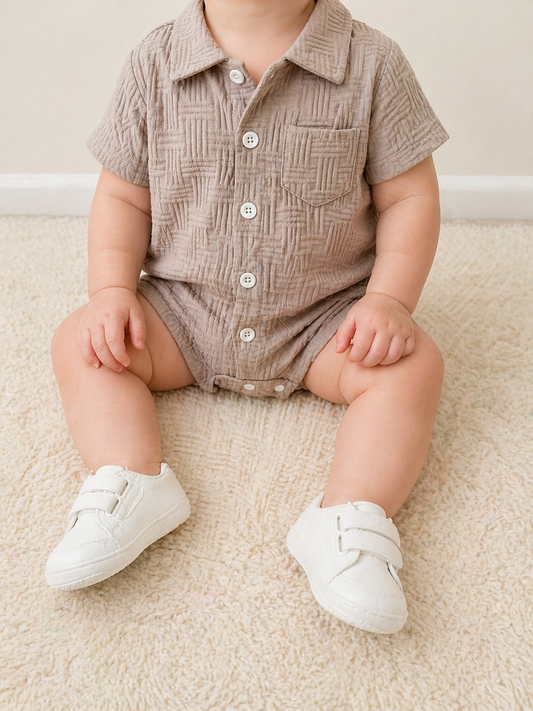 A baby in a Tiny Tot Bundles Sandstone Textured Bubble sits on a soft, light carpet with legs spread out, face not visible.