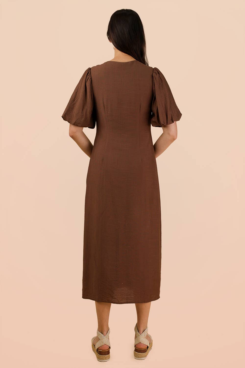 Back view of the brown Mocha Front Tie Midi Dress with puff sleeves, worn with espadrille wedge sandals.