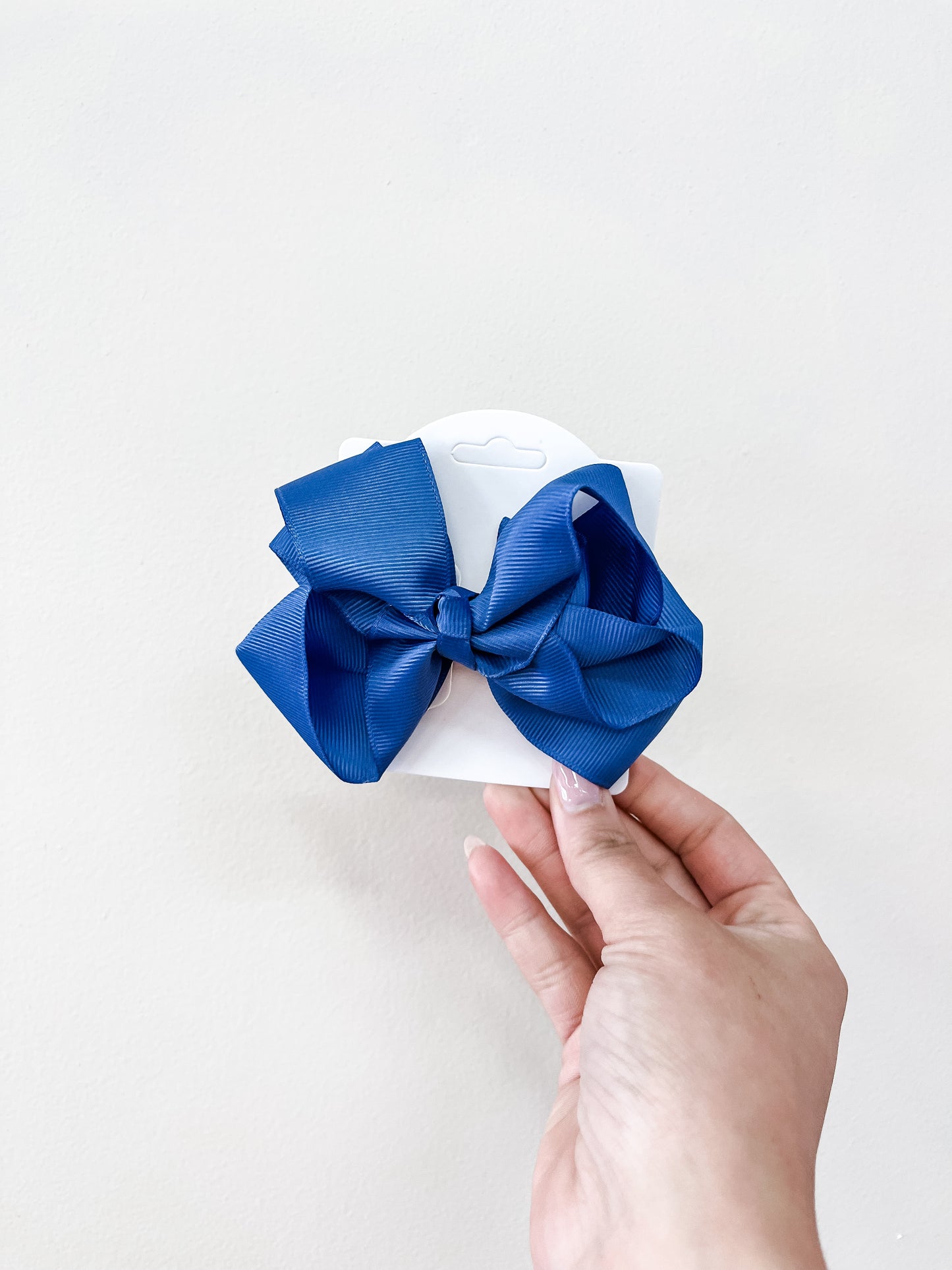 A hand holds a white card featuring funteze's Classic Boutique Bow—a large, neatly tied blue ribbon—against a plain light background.