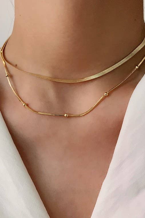 A person wears the Dainty Layered Tarnish Free Necklace, featuring two delicate gold-tone layers: a flat chain and a second chain with small spaced beads.