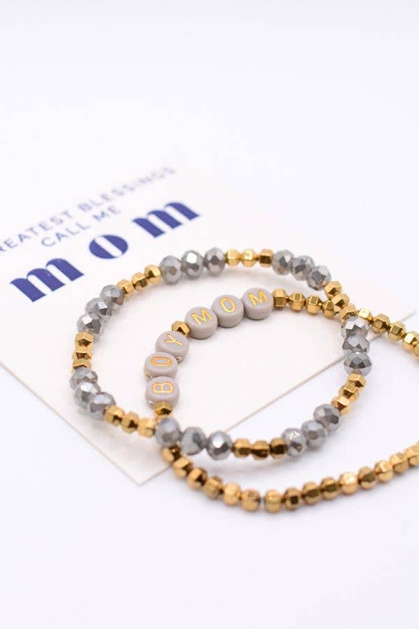 Two beaded bracelets from Two and Crew - Faith Based Jewelry & Gifts’ Boy Mom Bracelet Set—one gold and gray, the other featuring gray beads spelling out DIY MOM—are displayed on a card that partially reads, “Greatest Blessings Call Me Mom.”.