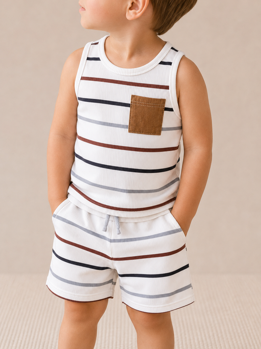 A young child models the Tiny Tot Bundles Neutral Stripe Tank Set—featuring a white sleeveless top with horizontal black, brown, and rust stripes plus a brown chest pocket—standing hands-in-pockets against a neutral backdrop.