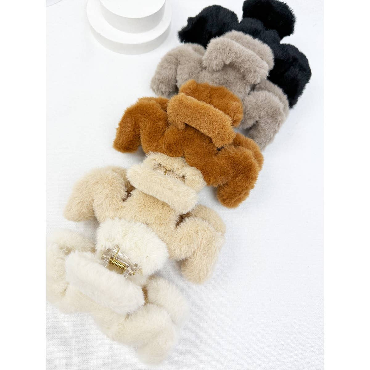 Five Jumbo Fur Wavy Hair Claw Clips by Love and Repeat in cream, beige, brown, gray, and black are arranged in a line on a white surface. Each clip is covered in plush faux fur.