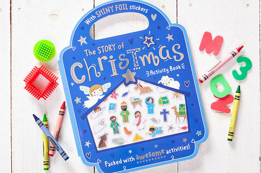 The Story of Christmas Activity Book by BroadStreet Publishing Group, LLC, featuring shiny stickers, is displayed on a white wooden surface surrounded by crayons, foam numbers, and textured toys.