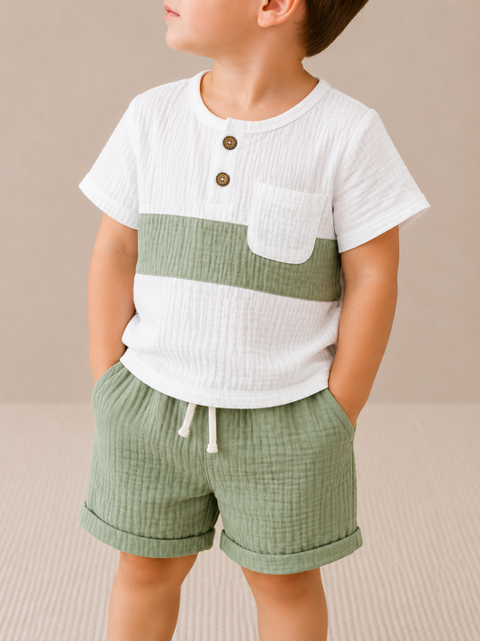 A young child models the Tiny Tot Bundles Linen White & Green Set—featuring a white short-sleeve shirt with green stripe and matching green shorts—standing against a neutral background, looking to the side.