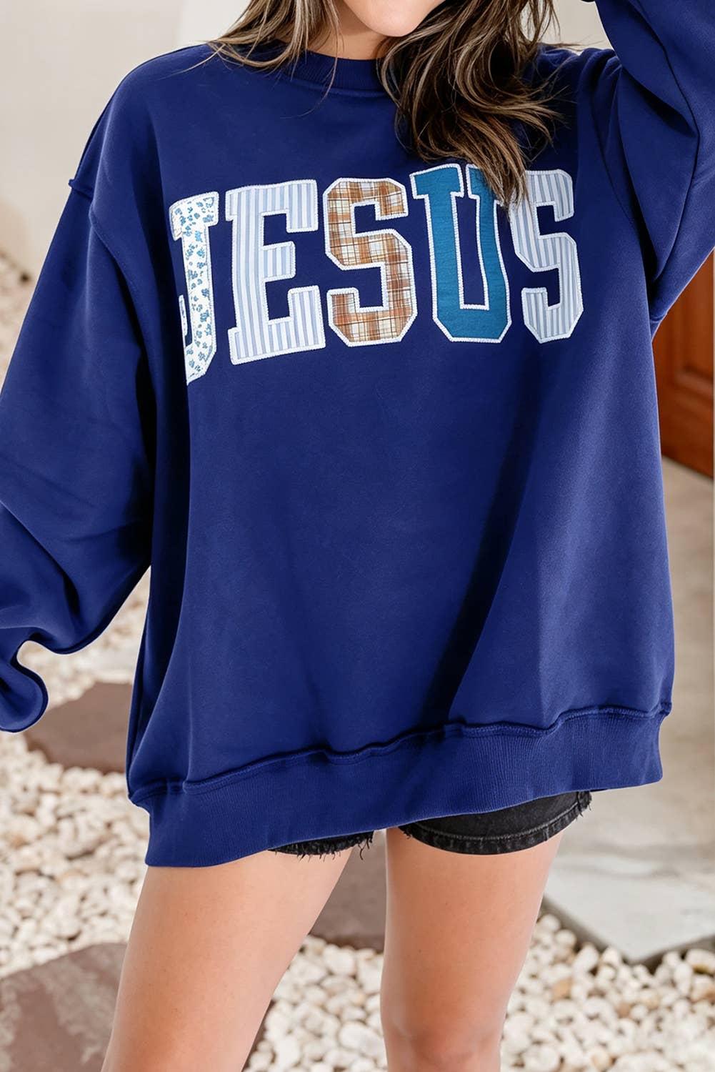 Little Daisy Closet Jesus Mock Neck Sweatshirt in navy blue with long sleeves and the word JESUS appliqued on the front in various patterned fabrics.