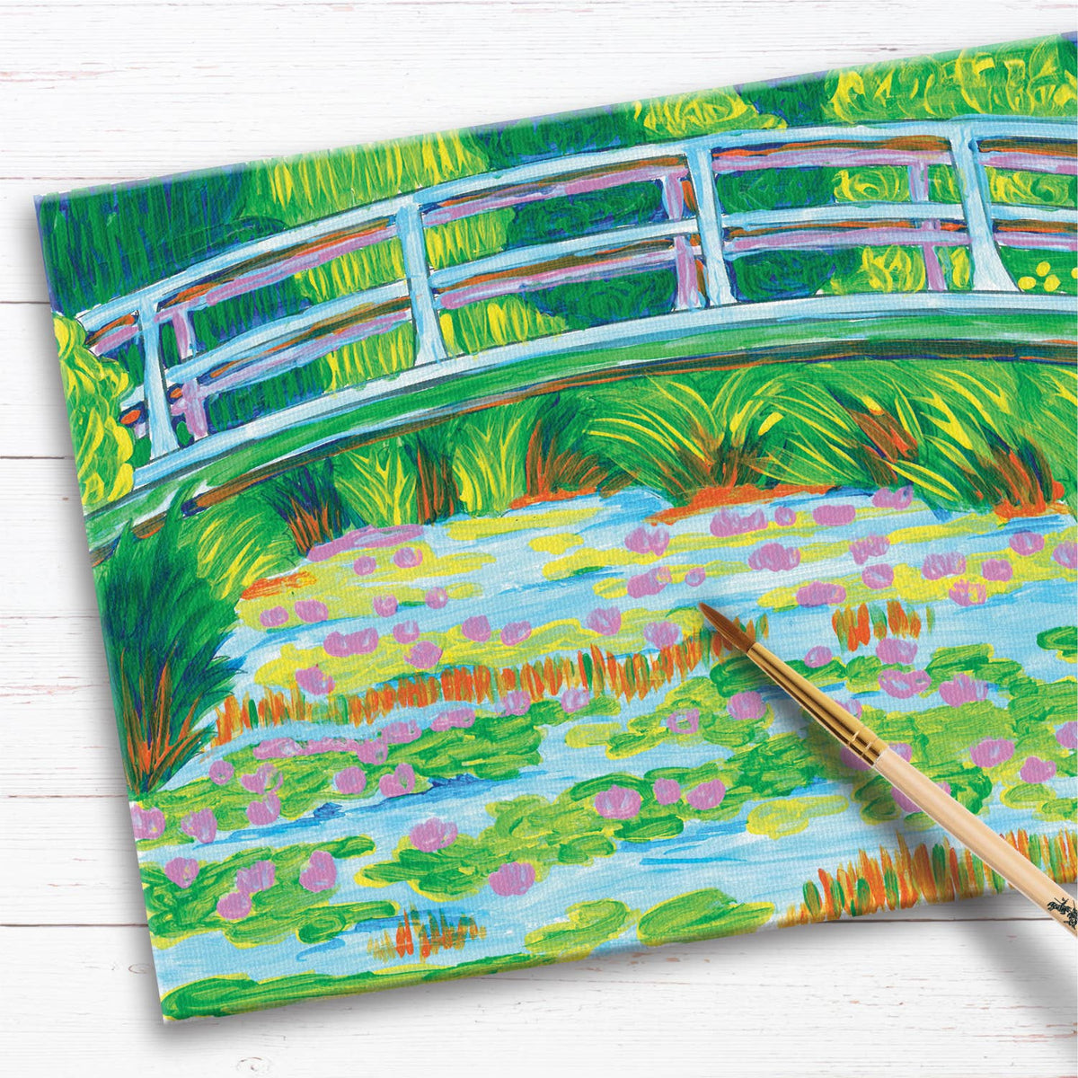 Experience the beauty of Monet with the Paint by Number Museum Series – The Japanese Footbridge by Faber-Castell / Creativity for Kids. This vibrant set features a Japanese-style bridge arching gracefully over a pond adorned with pink water lilies and surrounded by lush green foliage. A paintbrush rests beside the canvas, which sits atop a white wooden surface—inviting you to recreate this masterpiece and paint like the Masters.