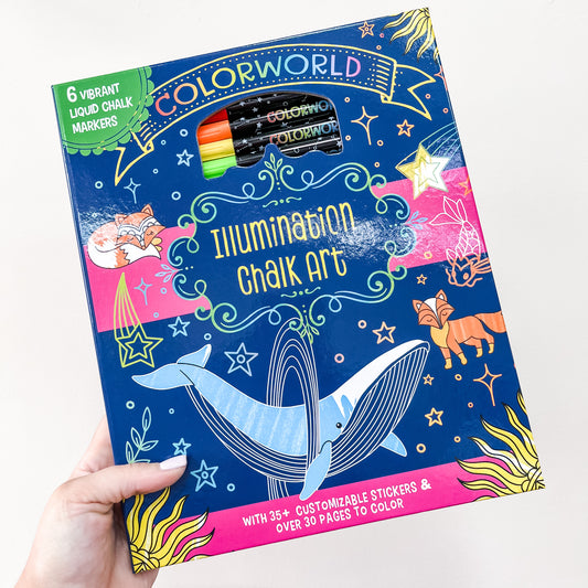 A hand holds the Color World - Illumination Chalk Art Activity Book by Simon & Schuster, with 6 liquid chalk markers, stickers, and coloring pages. The blue cover features a whale, fox, and stars.