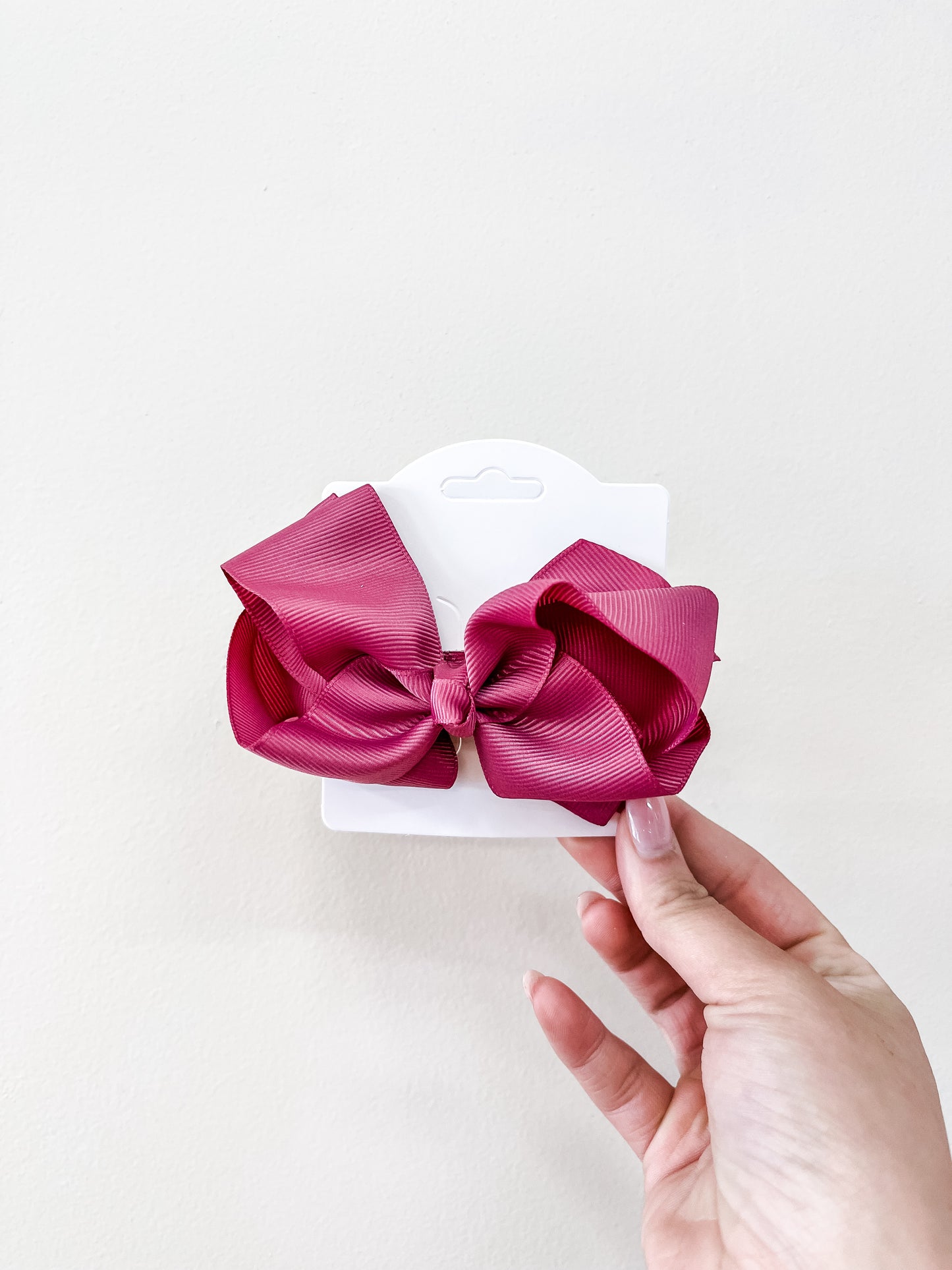 A hand holds a white card featuring the funteze Classic Boutique Bow—a large, pink, ribbed bow—set against a plain light background.