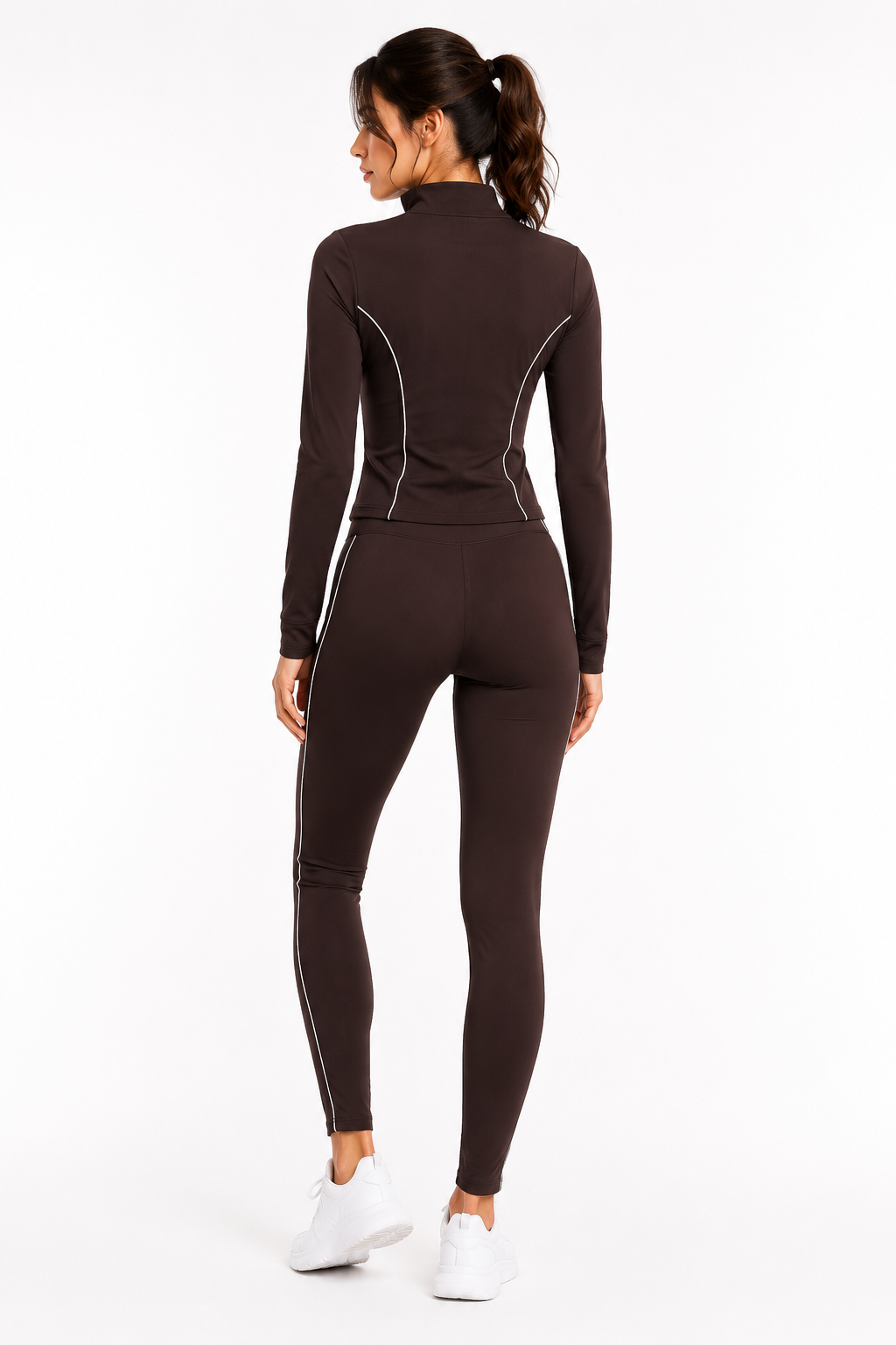 A woman wearing the Color 5 Chocolate Brown Active Set, featuring white piping, stands facing away and looks to her left. She has a ponytail and pairs the outfit with white sneakers against a plain white background.