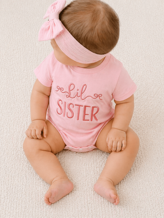 A baby in the Tiny Tot Bundles Lil Sister Pink Bubble sits on a light-colored carpet, wearing a pink headband and looking down with her hands on her legs.