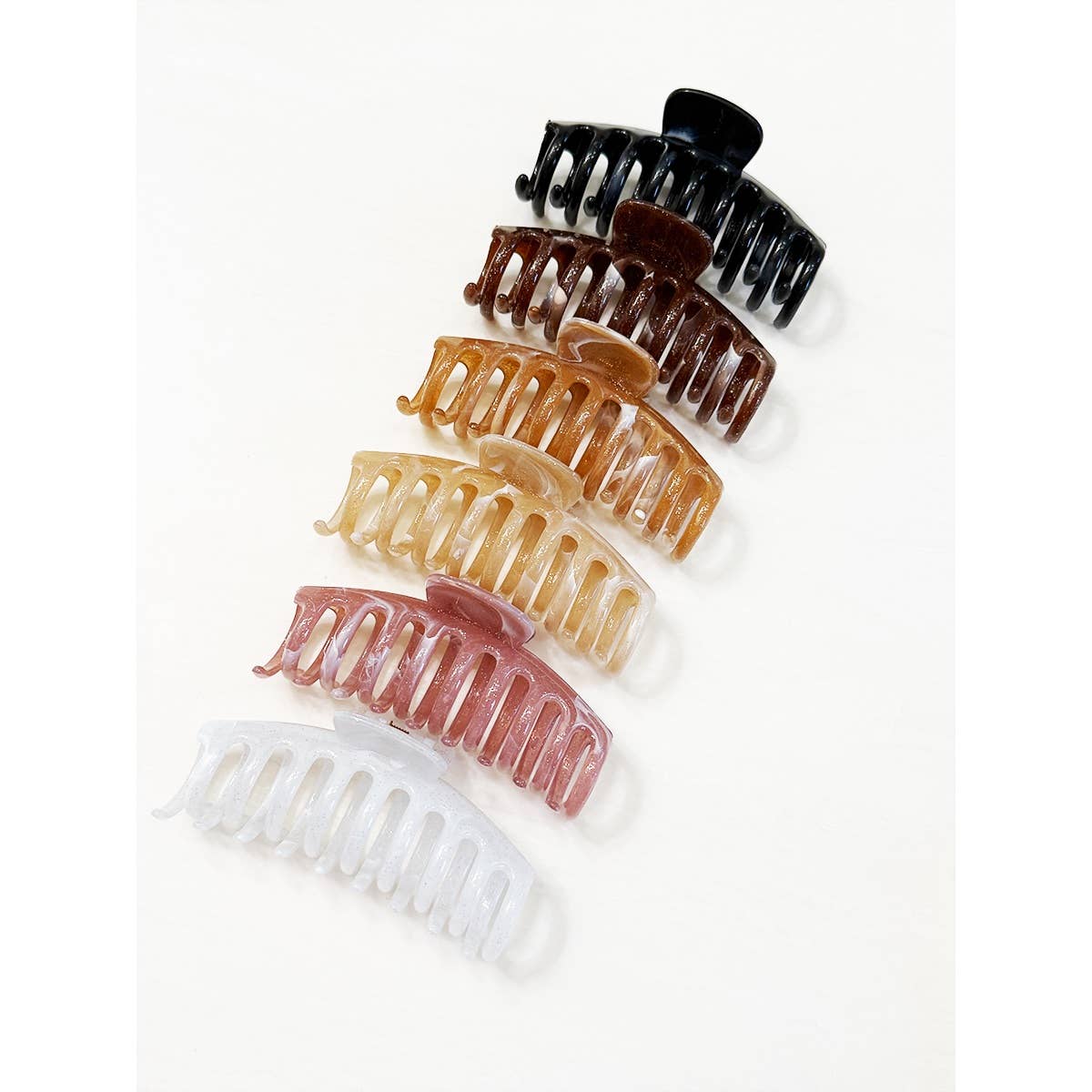 Seven Marbled Round Comb Hair Claw Clips by Love and Repeat, in black, brown, tan, gold, beige, pink, and white, are arranged in a vertical line on a white background.