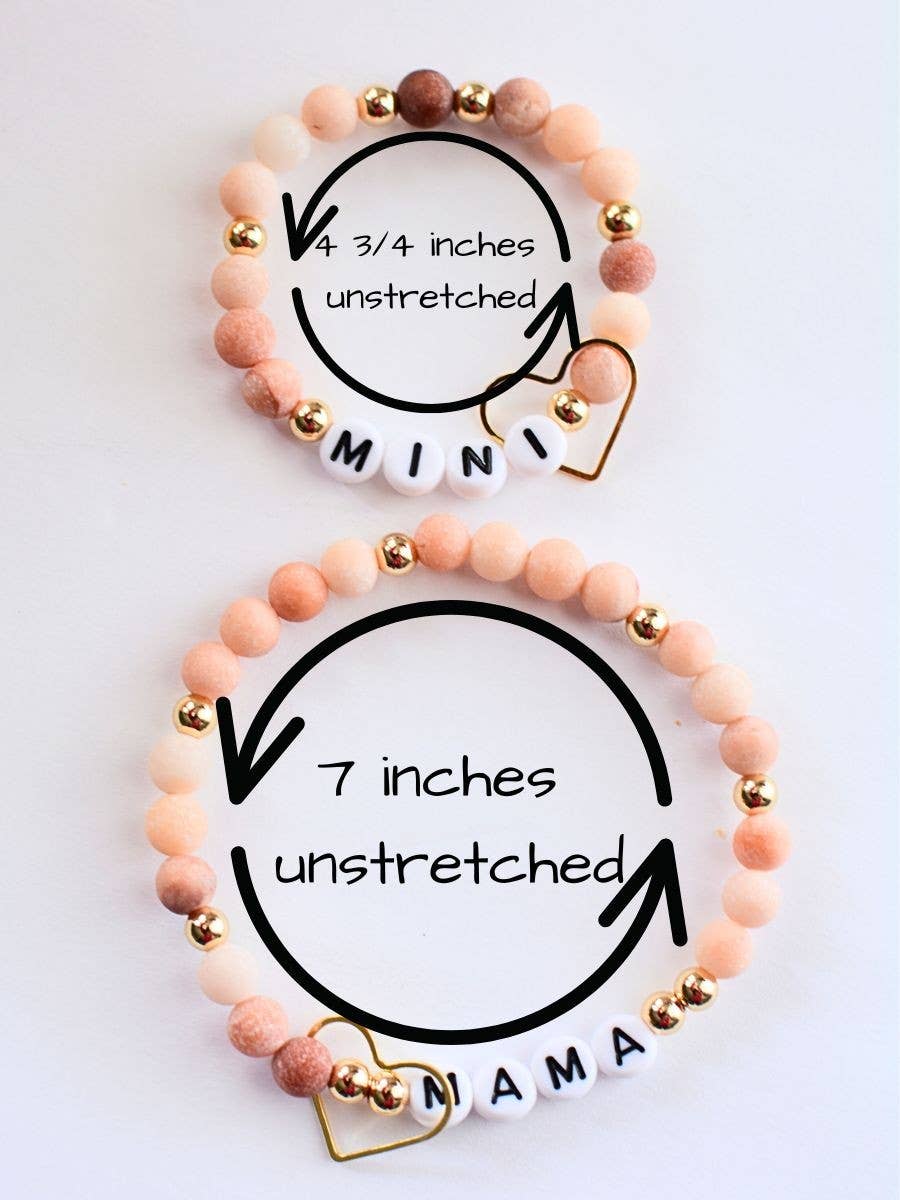 The Mama Mini Bracelet Set by Two and Crew - Faith Based Jewelry & Gifts includes two beaded bracelets, one labeled “MAMA” and the other “MINI,” in peach and gold tones with heart charms. The MINI bracelet measures 4 3/4 inches unstretched, while the MAMA bracelet measures 7 inches unstretched.