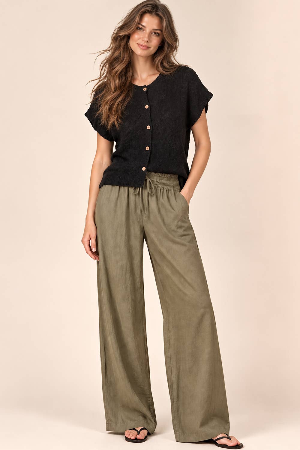 A woman wears a VERY J Black Knit Sweater Top with short sleeves and olive green wide-leg drawstring pants.