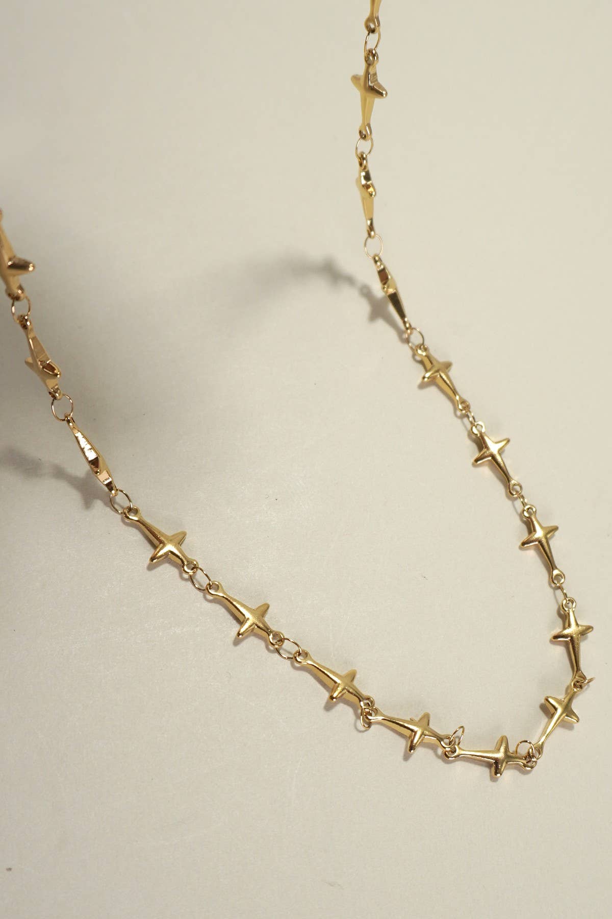 JOSSLYN by wall to wall Gold Dainty Cross Necklace featuring small, evenly spaced cross-shaped charms linked together, displayed on a light surface.