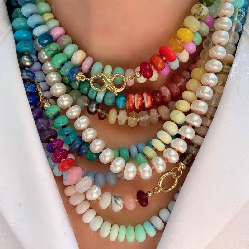 A close-up of a person wearing the JOSSLYN by wall to wall Natural Stone Glass Mixed Necklace, featuring colorful beads and pearls layered over a white shirt.