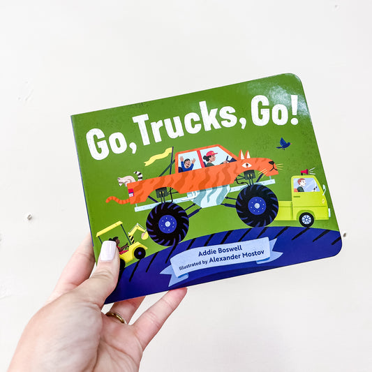 A hand holds the Go, Trucks, Go Book by Blue Star Press. The cover shows colorful cartoon trucks, including one with animal stripes and big wheels.
