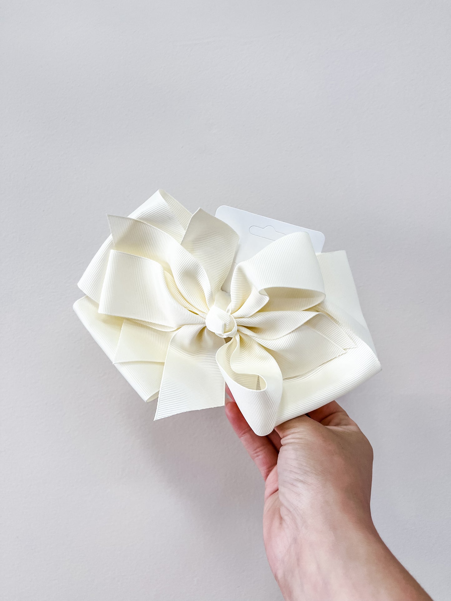 A hand displays the funteze Oversized Pastel Bows in cream against a plain light background.