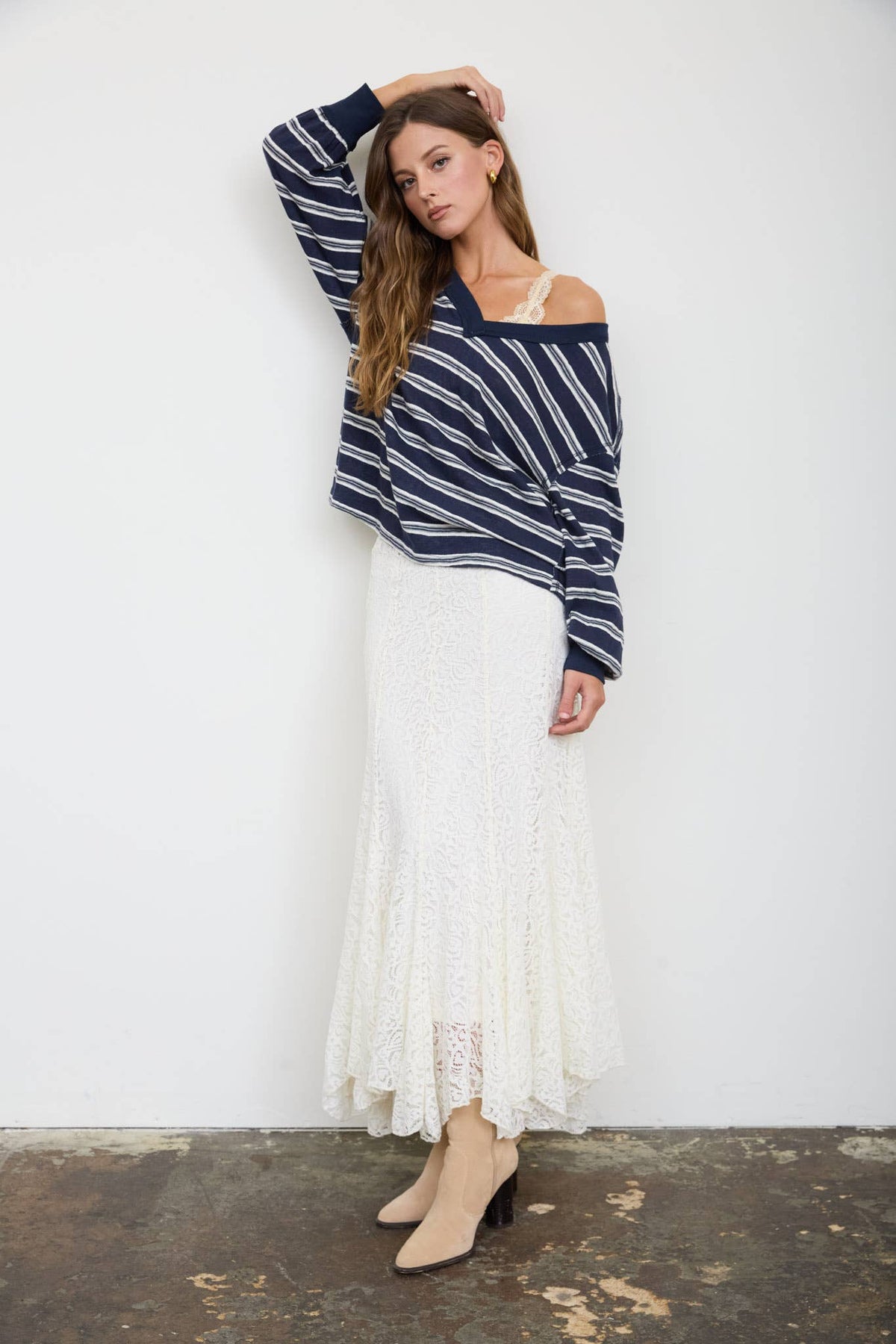 A woman wears a Blue Stripe V-Neck Long Sleeve top with a white lace maxi skirt and beige ankle boots.
