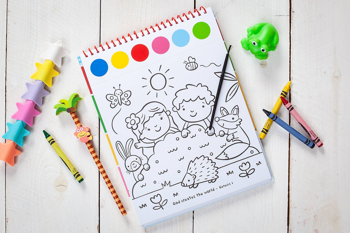 A Cozy Club Bible Friends Art Pad Book by BroadStreet Publishing Group, LLC featuring a coloring page with children, animals, plants, and the sun, surrounded by crayons, a paintbrush, a toy frog, star-shaped crayons, and a palm tree pencil.