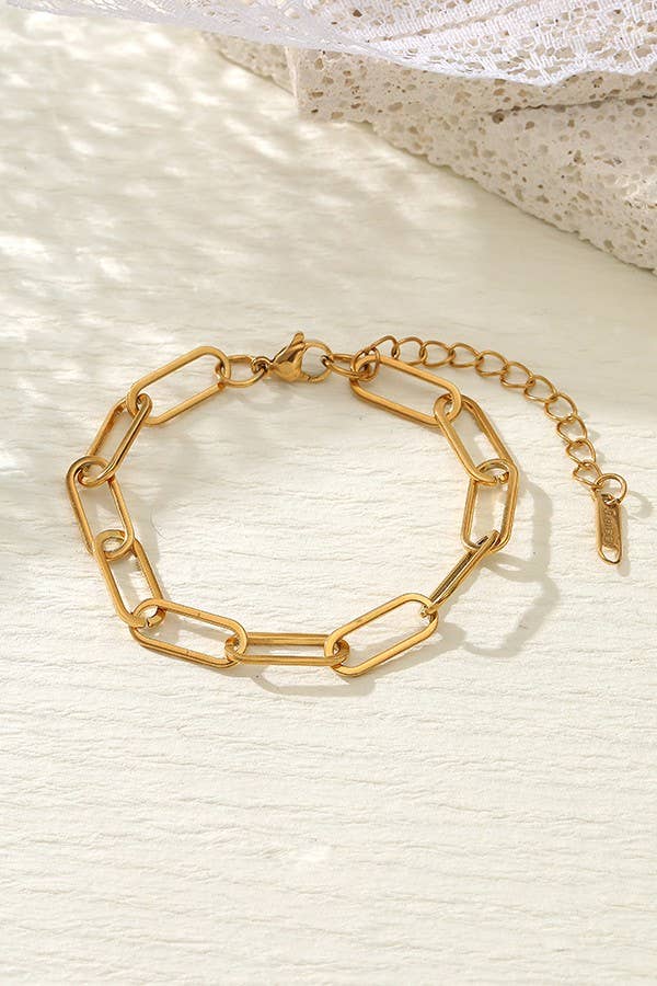 The Dainty Gold Bracelet by JOSSLYN by wall to wall, featuring an adjustable chain-link design, is displayed on a light-colored surface beside a delicate piece of lace fabric.