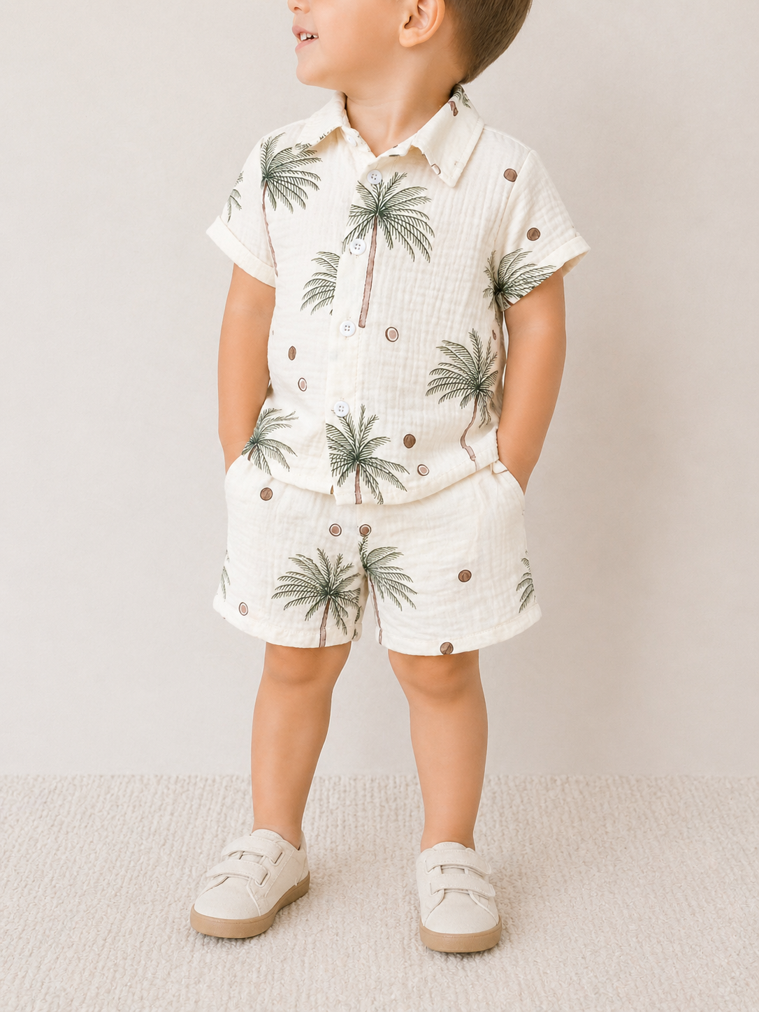 A young child models the Tiny Tot Bundles Palm Paradise Linen set—matching short-sleeve shirt and shorts with a palm tree and dot pattern—paired with light beige shoes, hands in pockets, looking to the side.