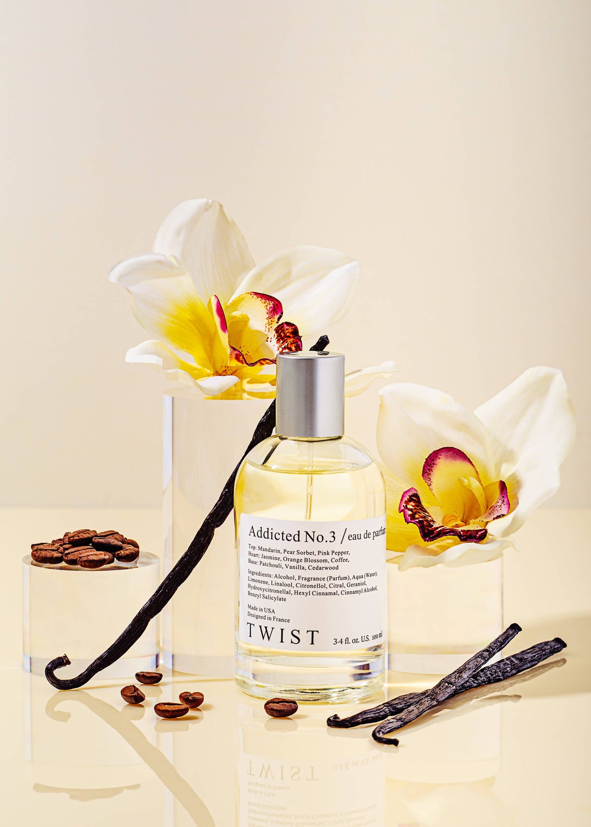 A bottle of House of Twist’s Addicted No.3 Perfume is positioned between two white orchids, surrounded by coffee beans and vanilla pods on a reflective surface, evoking the allure of a French fragrance. This long-lasting perfume for women combines elegance with irresistible charm.