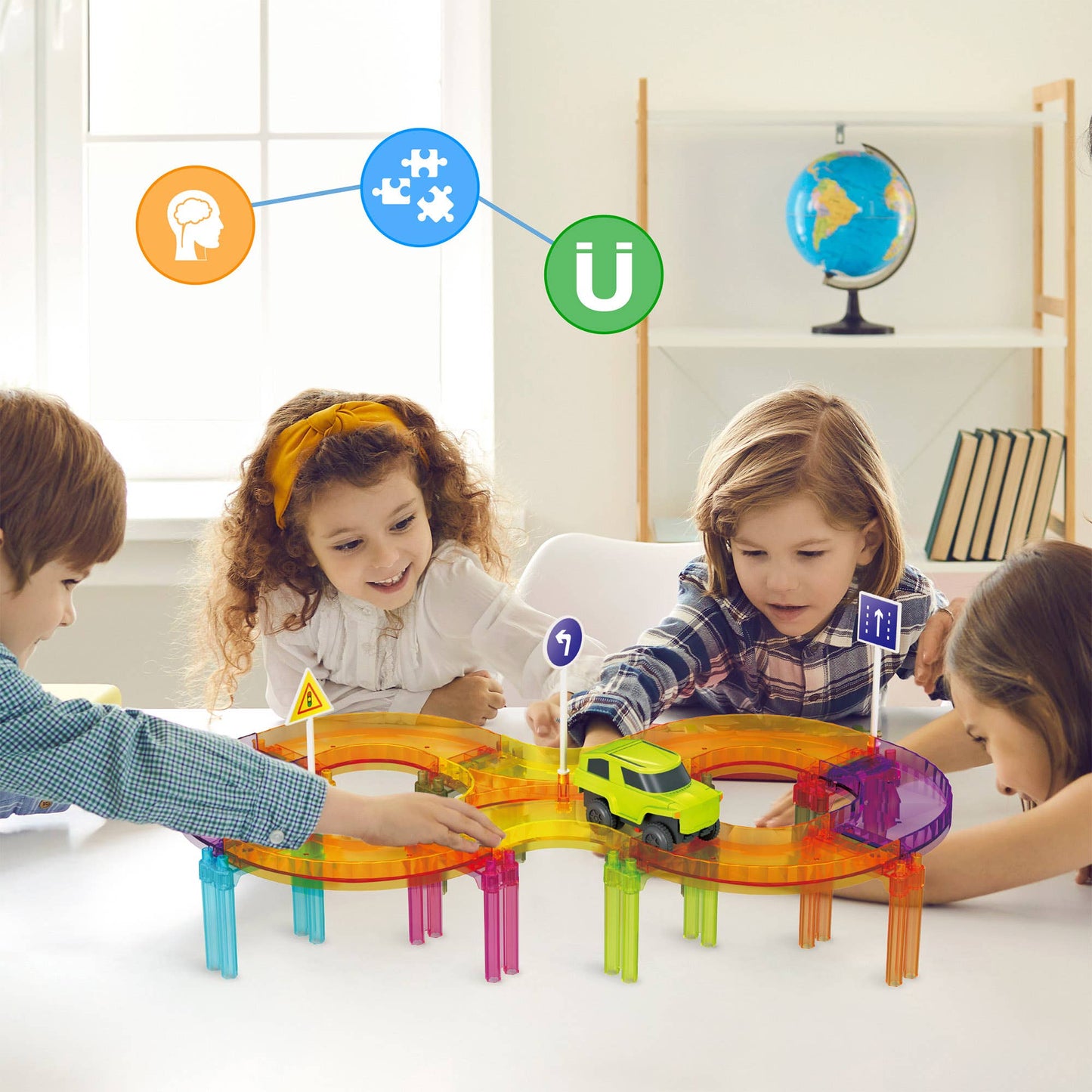 Four children play together with the PicassoTiles 40pc Travel Size Magnetic Tile Race Track Set on a white table in a bright room. Educational icons and a globe appear in the background.