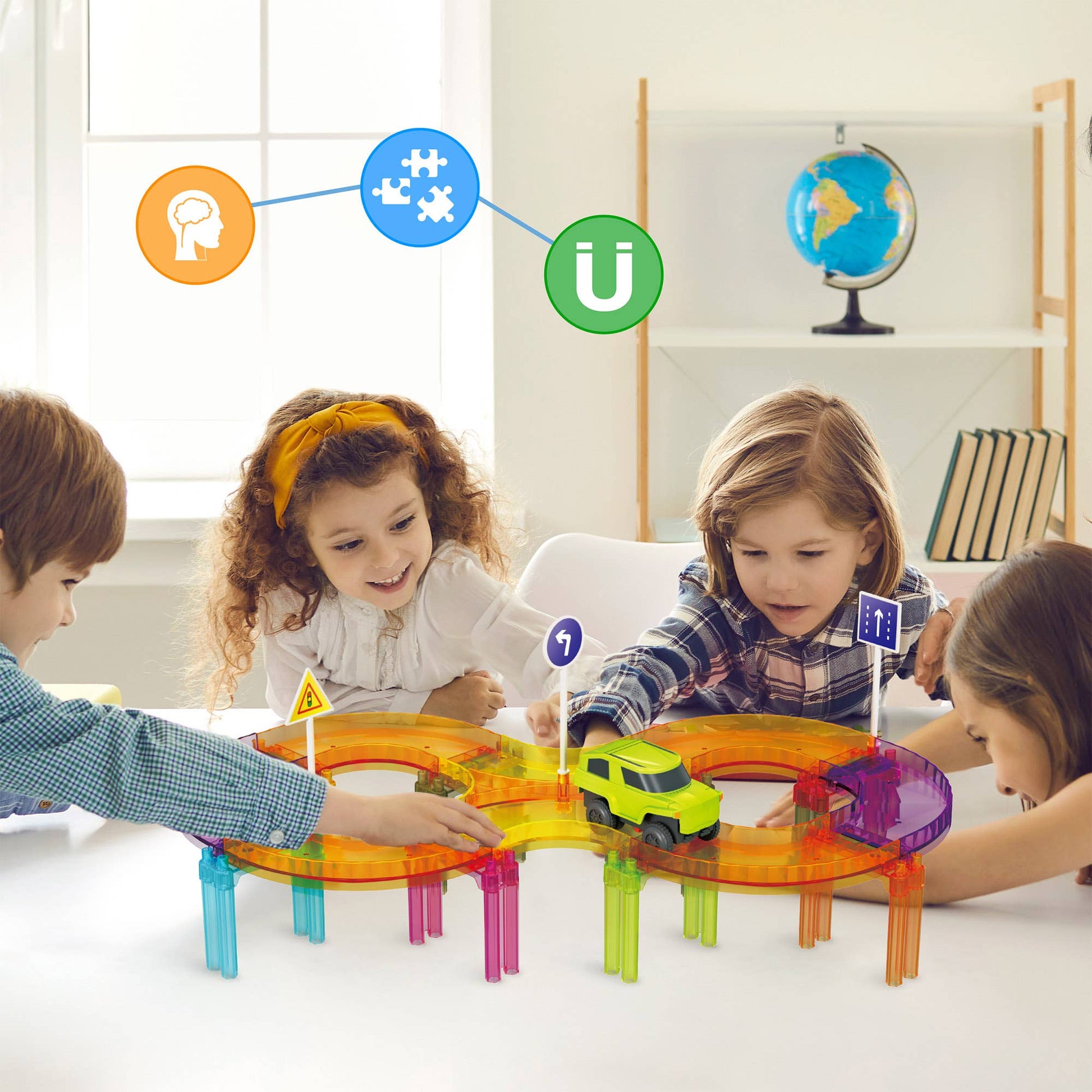 Four children play together with the PicassoTiles 40pc Travel Size Magnetic Tile Race Track Set on a white table in a bright room. Educational icons and a globe appear in the background.