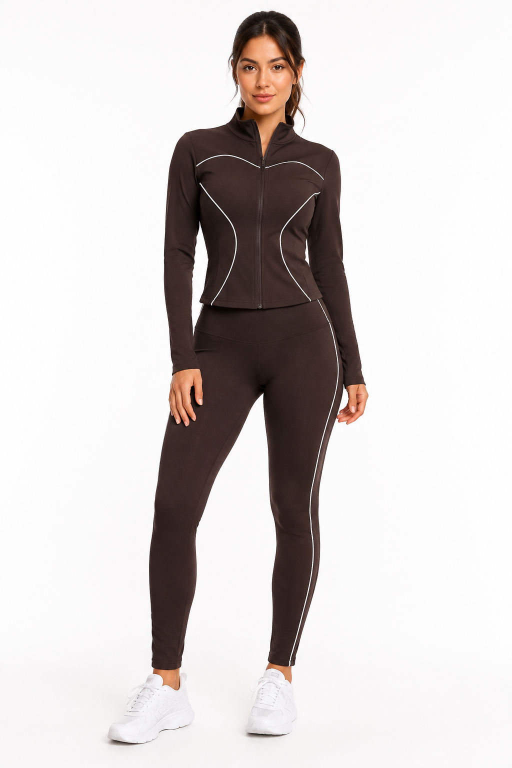 A woman stands in the Color 5 Chocolate Brown Active Set— a fitted athletic tracksuit featuring white piping, a zip-up jacket, and matching leggings. She pairs the outfit with white sneakers and smiles slightly against a plain white background.