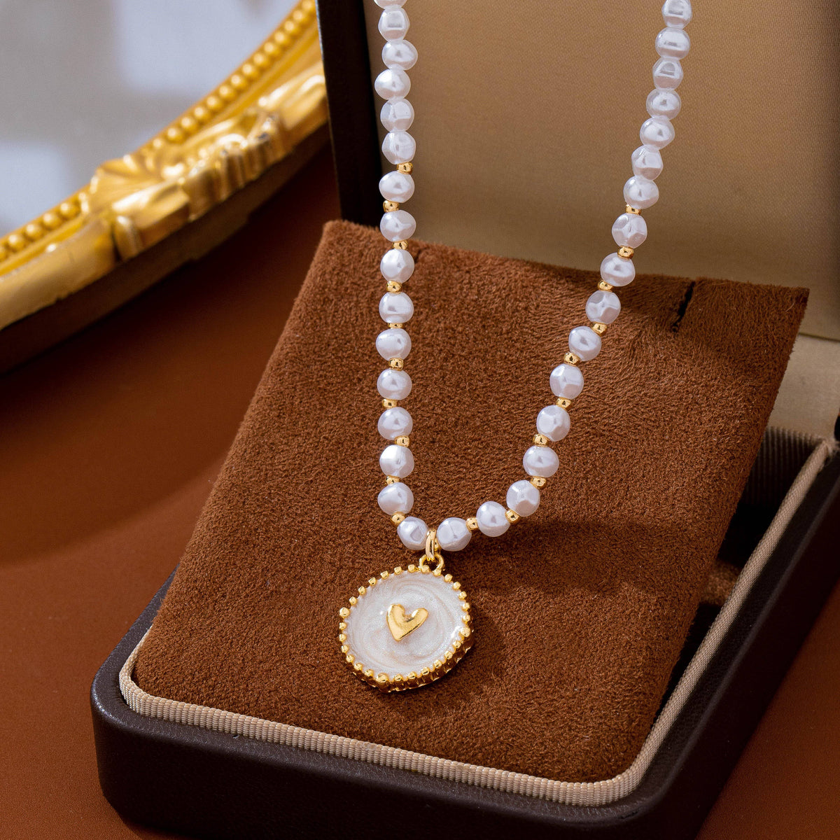 JOSSLYN by wall to wall Pearl Beaded Heart Charm Necklace featuring a string of small white pearls accented by gold beads, with a round pendant containing a gold heart at its center.