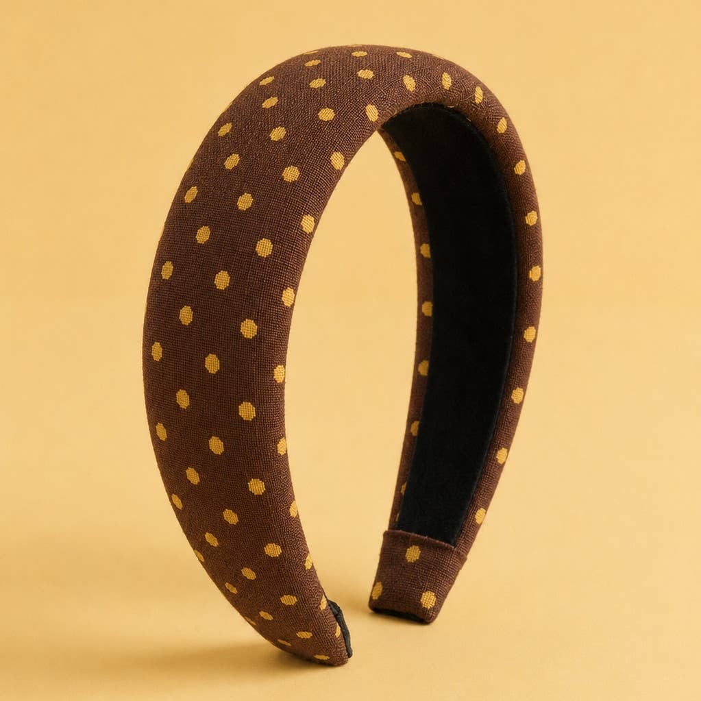 The JOSSLYN by wall to wall Padded Polka Dot Fabric Headband, featuring brown fabric with yellow polka dots, is positioned upright against a coordinating yellow background.
