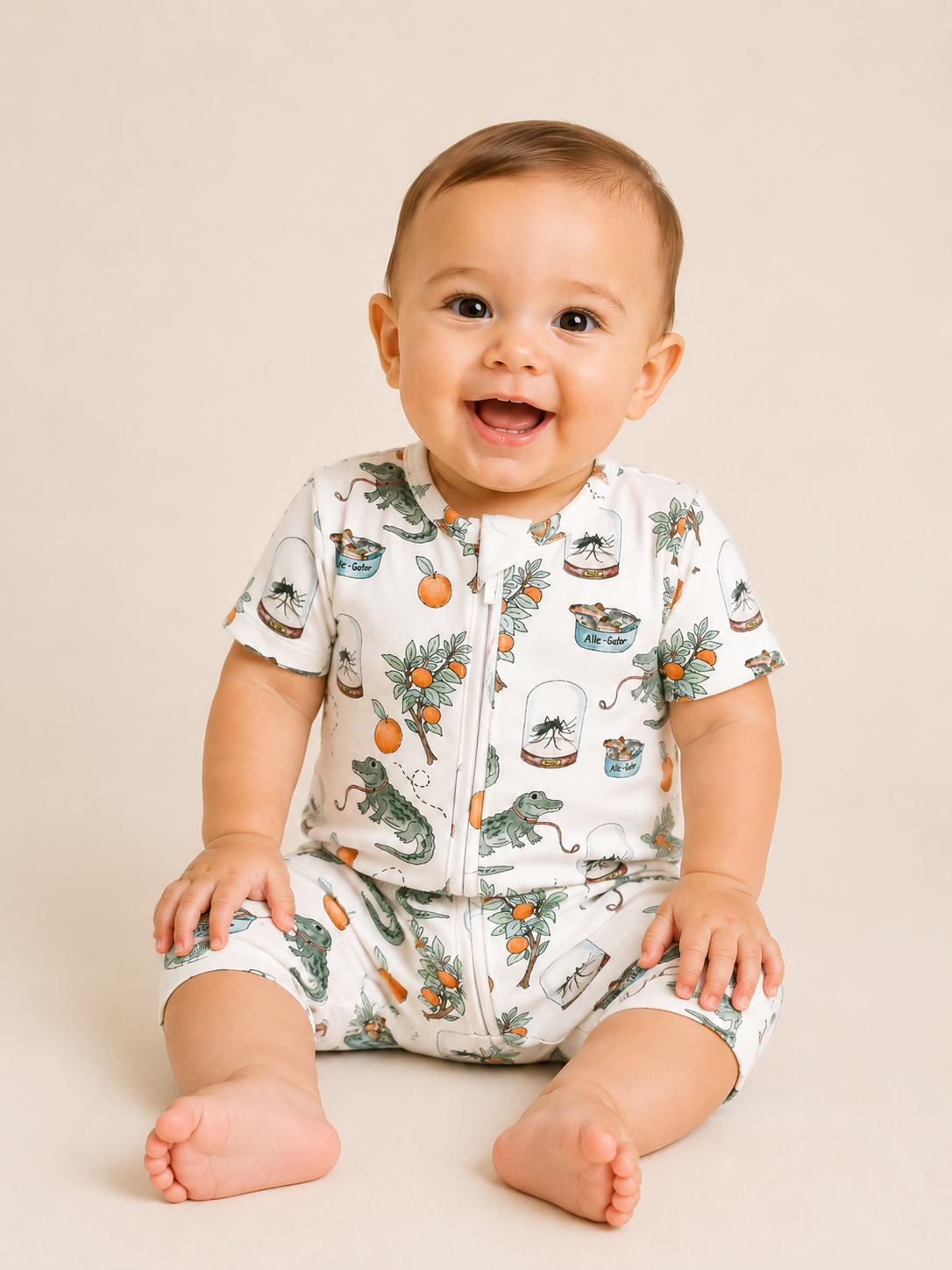 A smiling baby with short brown hair sits on a light surface, wearing the Tiny Tot Bundles Sunshine Swamp Short Zippy—an alligator, orange, and plant print onesie—and looks slightly upward.