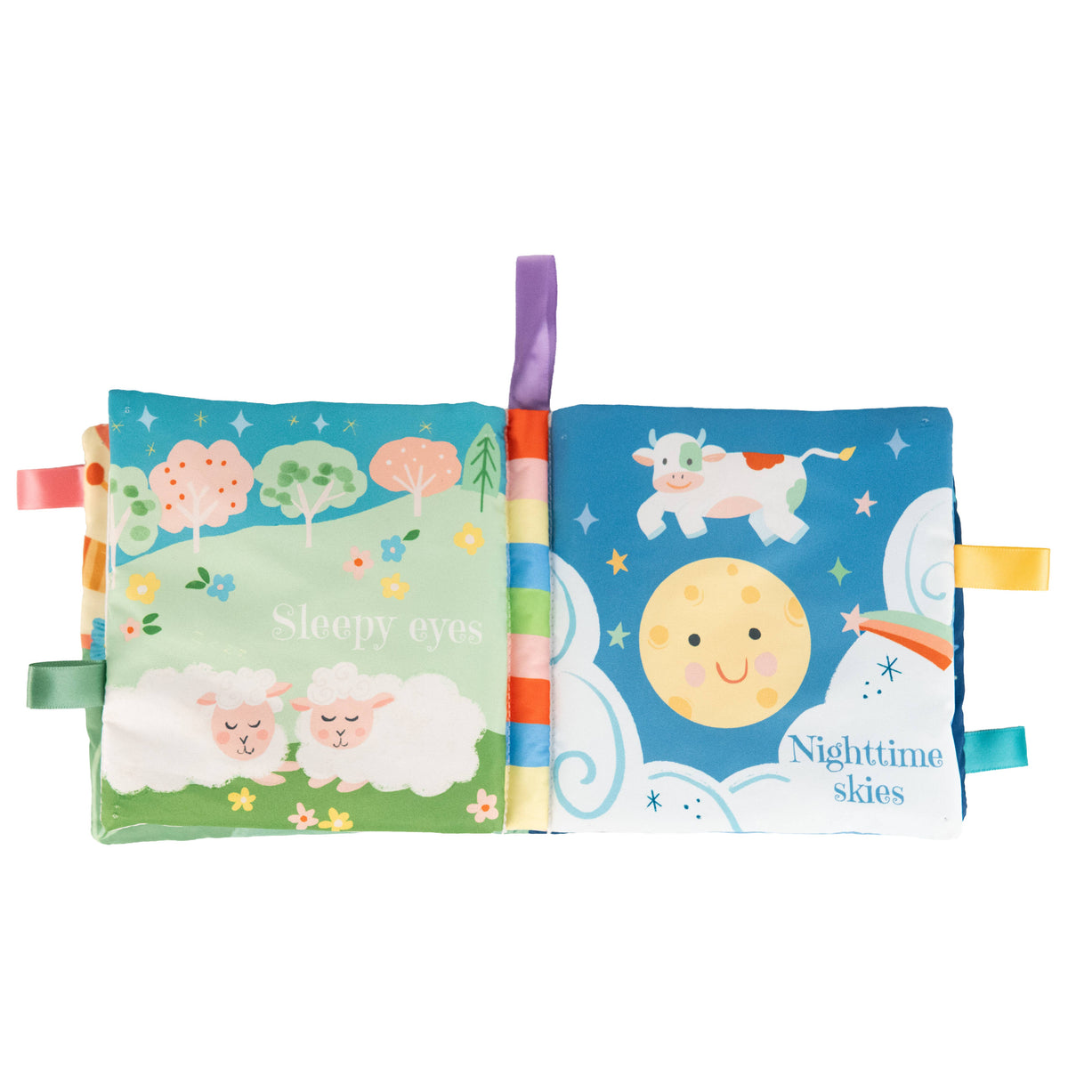 The Sweet Dreams Cloth Book by Cottage Door Press features two soft pages: the left displays two sleeping lambs, dreamy trees with sleepy eyes, and the right shows a smiling moon and cow against nighttime skies. Colorful ribbon tags edge the book, making this charming sensory cloth book ideal for little hands to explore during storytime.