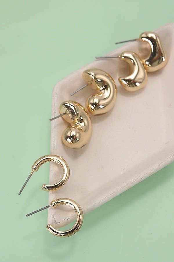 Three gold-toned puffy Bubble Hoop Trio Earrings and two small, thin gold hoop earrings arranged on a pale triangular tray.
