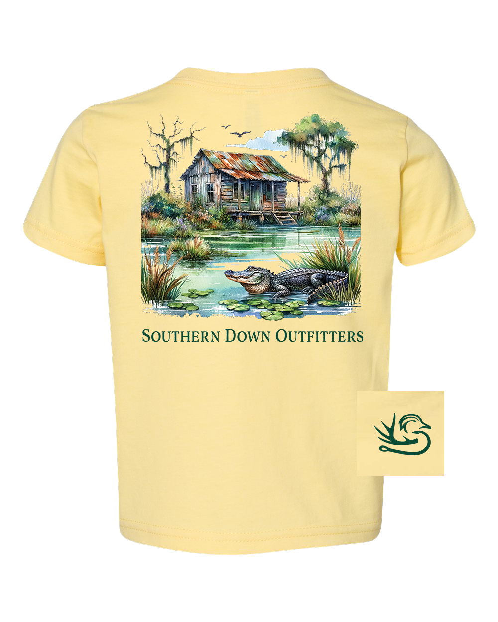 Swamp Shack Toddler Tee by Southern Down Outfitters features a yellow design with an illustrated alligator by a pond, old wooden cabin, trees, birds, "SOUTHERN DOWN OUTFITTERS" text, and the brand logo in the bottom right corner.