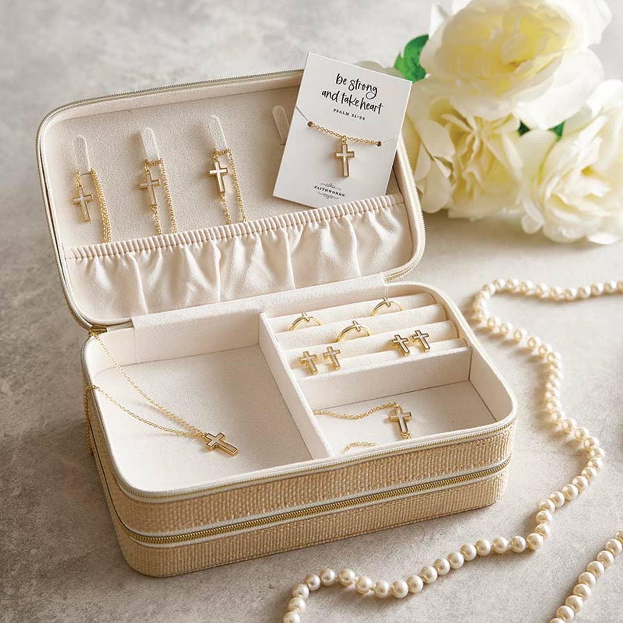 A Mother of Pearl Cross Filled Display by Faithworks from Creative Brands showcases gold cross necklaces and earrings, a card reading “be strong and take heart,” white roses, and a pearl necklace on a light surface.