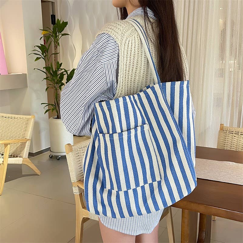 A person wears a blue and white striped Striped Blue Double Pocket Tote by JOSSLYN by wall to wall with an exterior pocket over their shoulder.