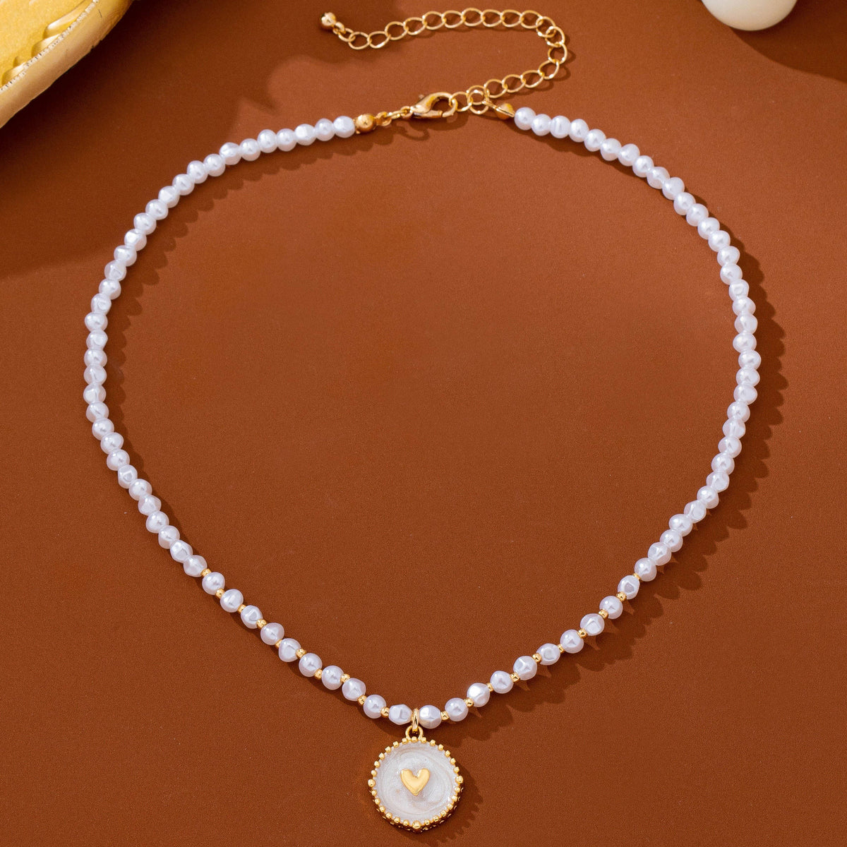 JOSSLYN by wall to wall Pearl Beaded Heart Charm Necklace featuring a string of white pearl beads with a round pendant and a small gold heart at the center.