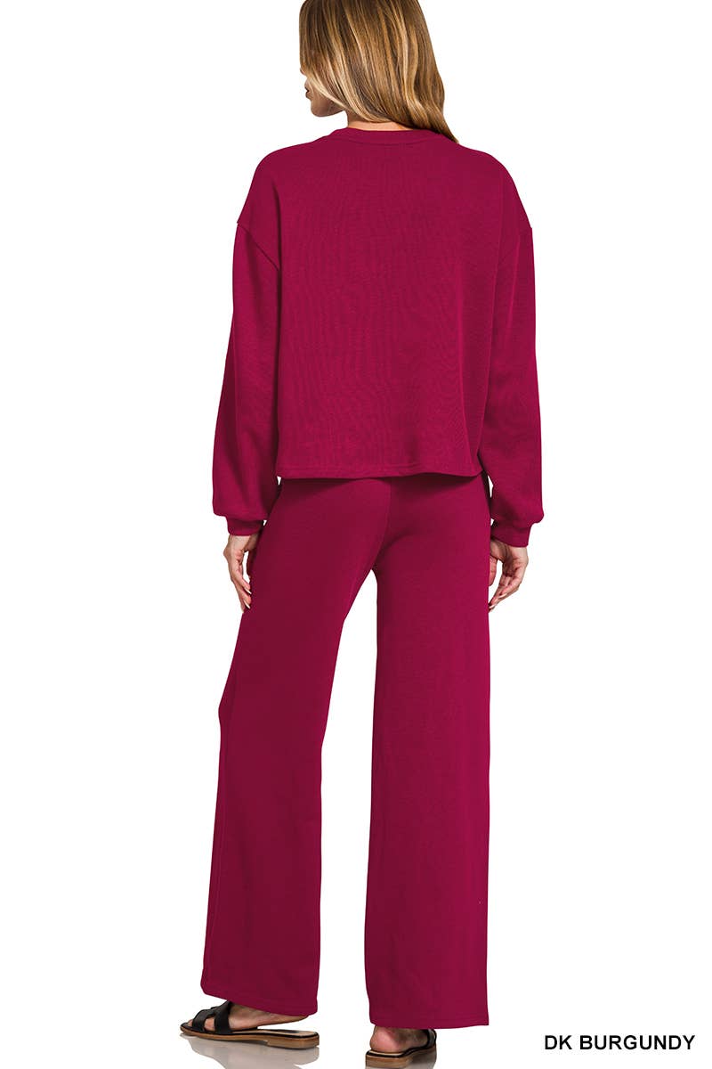 A woman wears a 42POPS Red Ribbed Pullover Pant Set featuring a long-sleeved ribbed pullover and matching wide-leg pants in dark burgundy.