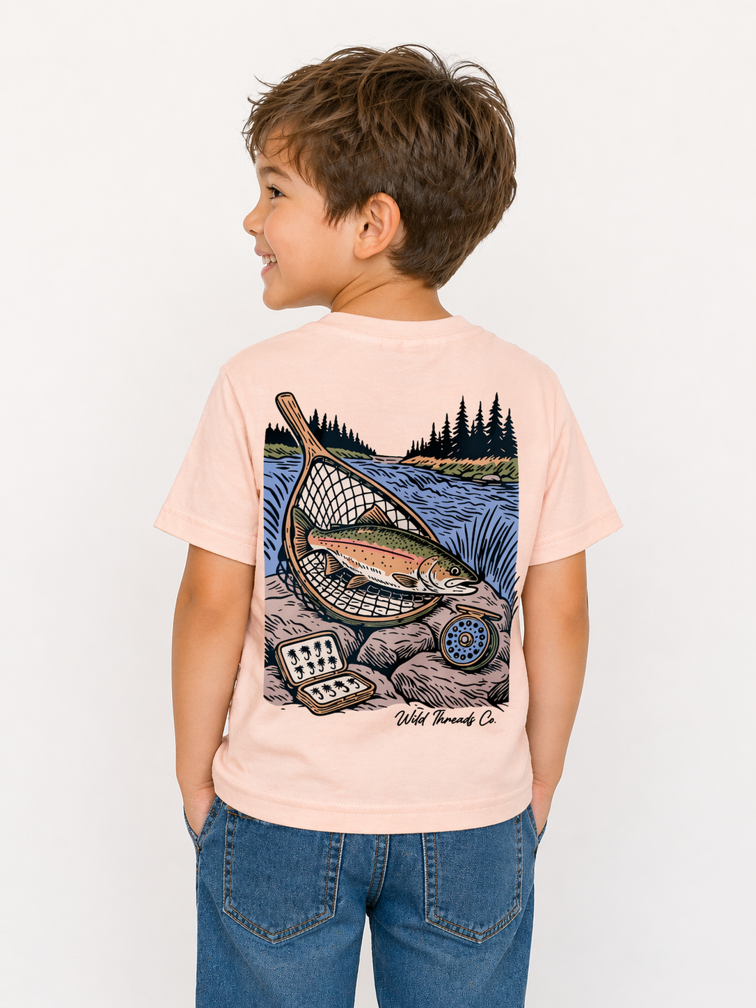 A young boy in blue jeans and a Wild Threads Co River Catch T-Shirt looks to the side. The shirt has a fish-in-net by a river illustration, complete with fishing gear and trees in the background.