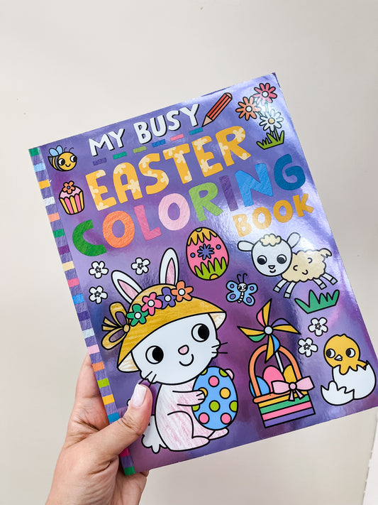 A hand holds Tiny Tot Bundles’ My Busy Easter Coloring Book with a bunny in a hat, Easter eggs, basket, chick, lamb, and flowers on the purple cover.