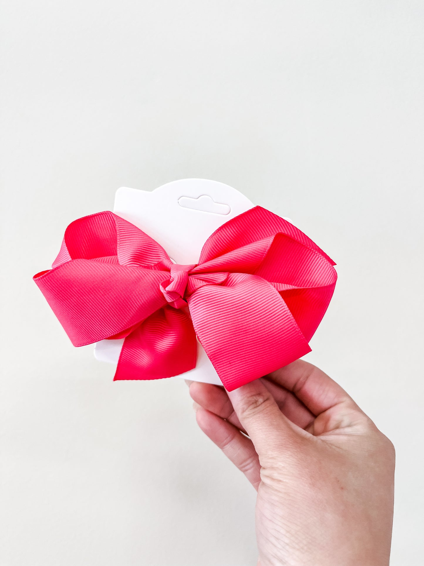 A hand holds a white card featuring an Oversized Pastel Bow in bright pink from funteze, set against a simple light background.