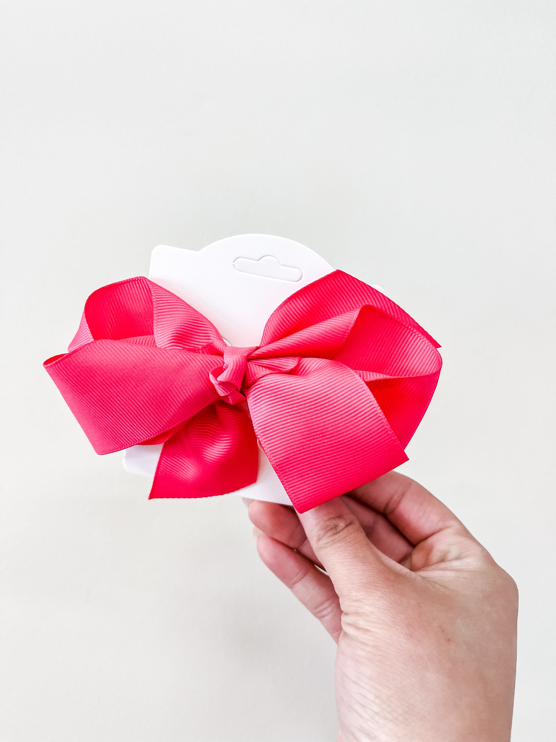 A hand holds a white card featuring an Oversized Pastel Bow in bright pink from funteze, set against a simple light background.