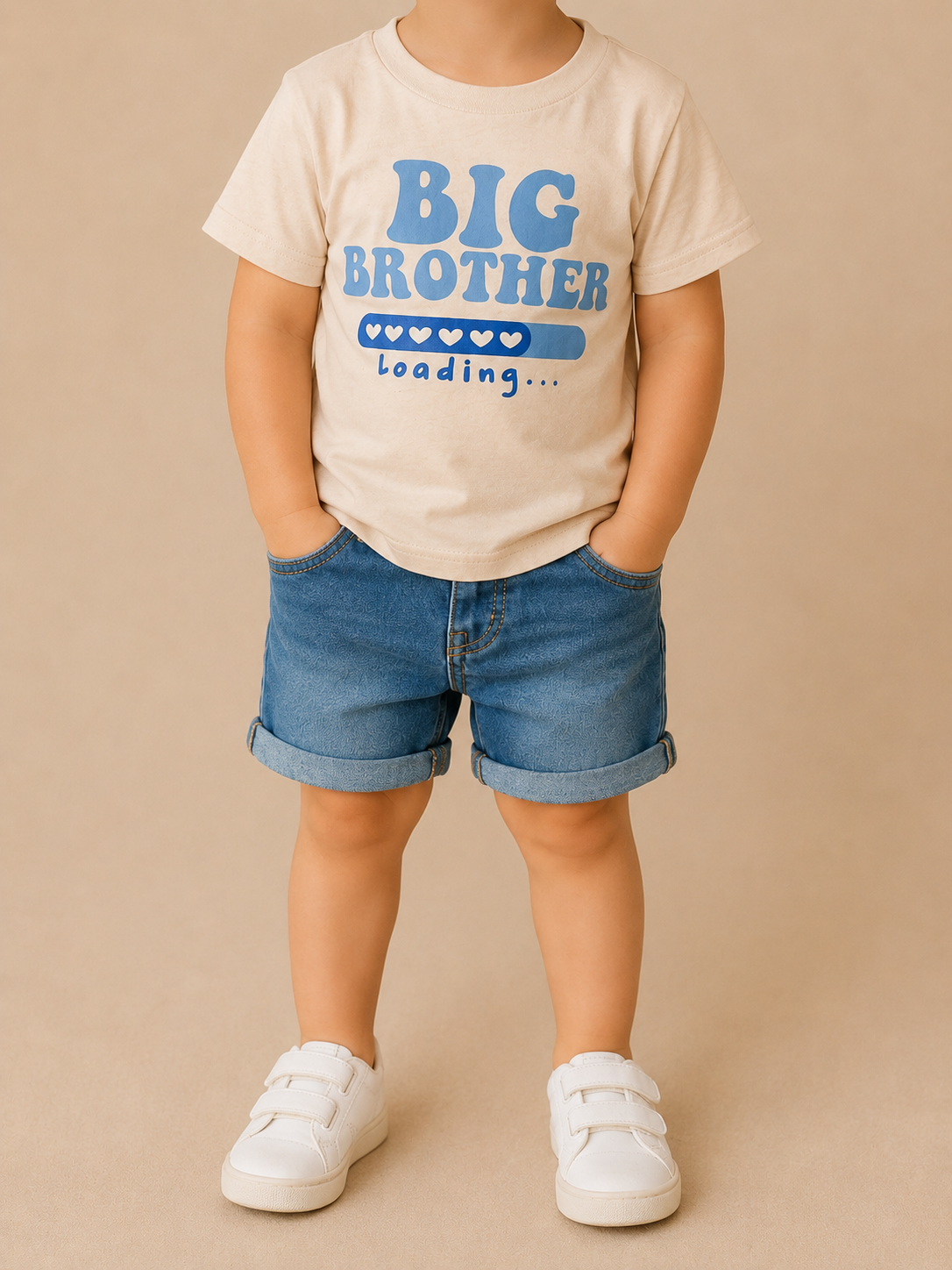 A young child wears the Big Brother Loading Tee by Tiny Tot Bundles, styled with denim shorts and white sneakers, standing against a beige background.