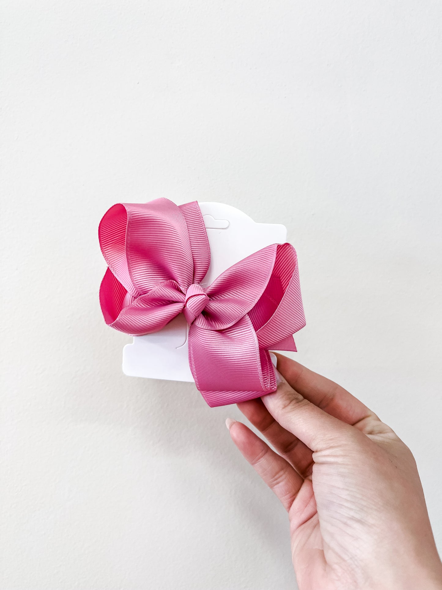 A hand holds a white card featuring the Classic Boutique Bow by funteze—a large pink ribbon bow—against a plain, light background.