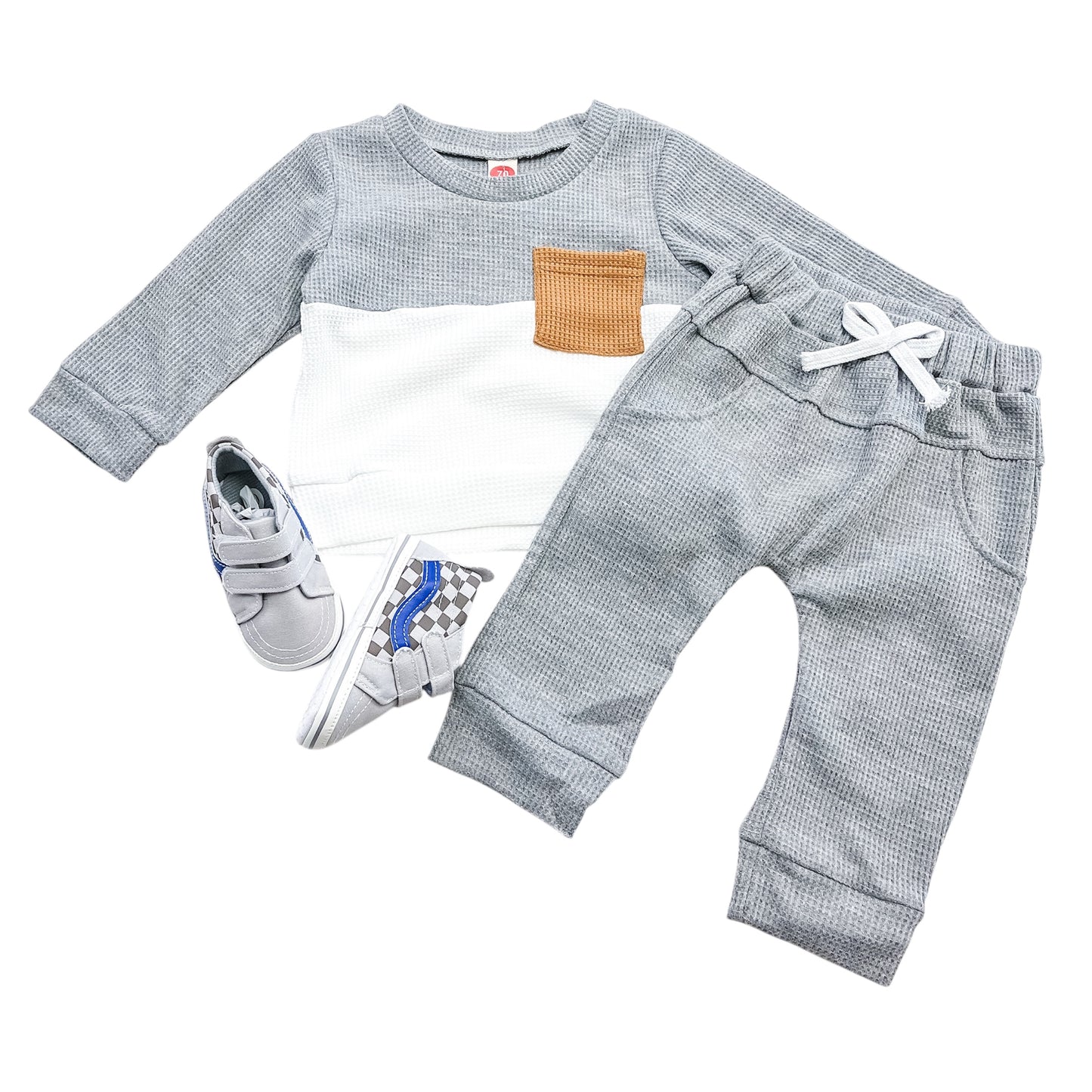 The Tiny Tot Bundles Greystone Waffle Set includes a grey and white long-sleeve shirt with a tan pocket, grey pants featuring a white drawstring, and grey slip-on sneakers accented with blue and white.