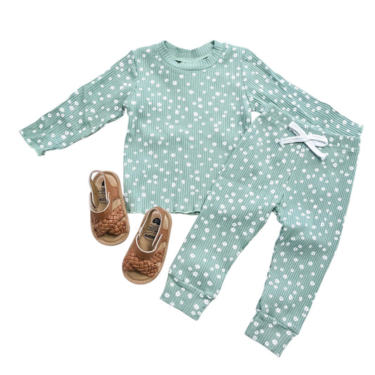 The Tiny Tot Bundles Sage Daisy Ribbed Set, featuring a green long-sleeve shirt and pants with white polka dots, is paired with brown woven sandals for children and displayed on a white background.